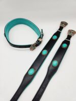 A teal and black leather belt with silver buckle detailing, lying flat and open. Near it is another matching belt adorned with turquoise oval decorations, reminiscent of a Leather Dog Collar- Natural Turquoise Stone. Both pieces showcase intricate craftsmanship and a contrasting color scheme.