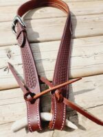 A close-up image of a brown leather Western-style belt with intricate woven detailing, lying on a wooden surface. The belt features a silver buckle and a piece of antler tied to it with leather straps.