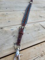 A leather dog leash with silver buckle and turquoise-colored accents lies on a wooden surface. The leash features stitched detailing and a sturdy metal clip at one end for attaching to a collar.