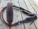 A handcrafted leather horse tack with intricate tooled floral designs and turquoise accents is displayed on a wooden surface. The detailed craftsmanship highlights a blend of traditional Western and Native American artistic influences.