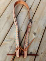 A leather dog collar with blue stitched accents and a metal buckle is laid out on a wooden surface. The collar has an attached leash loop with an elongated wooden toggle. The natural wood planks underneath have a rustic appearance with visible grain and knots.