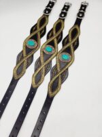 Three black leather wristbands featuring intricate gold thread patterns and turquoise stone accents in the center are aligned parallel on a white background. Each wristband has an adjustable buckle for closure.