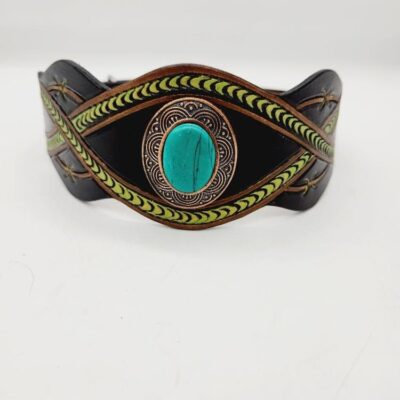 A leather bracelet with intricate green and black patterns and a central turquoise stone. The design features woven elements and decorative embellishments on the sides. The background is plain white.