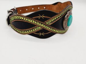 A black leather dog collar with intricate green leather designs and a turquoise stone centerpiece. The collar has a metal buckle and stitching details on the edges. The background is plain white.