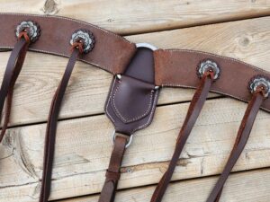 A brown leather horse bridle with decorative conchos and straps laid out on a wooden surface. The bridle features silver hardware and multiple leather ties. The wooden background provides a rustic appearance.