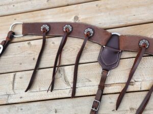 A leather horse bridle is laid out on a wooden surface. It has intricate stitching, metal rings, and straps with buckles. The bridle is designed for equestrian use, showcasing craftsmanship and durability.