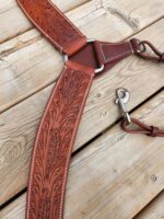 Close-up photo of a handcrafted brown leather horse breast collar with intricate floral tooling displayed on a wooden surface. It includes a metal ring and a snap hook for securing. The detailed stitching enhances the quality and craftsmanship of the piece.