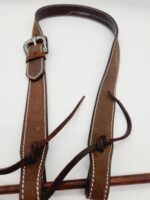 A brown leather belt with white stitching and a silver buckle is lying on a white background. The belt has leather strings tied around it and is slightly coiled at the top.