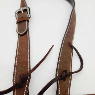 A brown leather belt with white stitching and a silver buckle is lying on a white background. The belt has leather strings tied around it and is slightly coiled at the top.