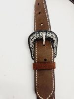 A close-up of a brown leather belt with white stitching. The belt features an intricately designed silver buckle with floral engravings. The belt is looped through a matching leather belt keeper. The background is plain and white.