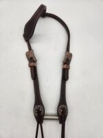 A brown leather horse bridle featuring intricate stitching and two intricately designed metal buckles is laid flat on a white surface. The bridle has padded sections for comfort and decorative accents near the buckles.