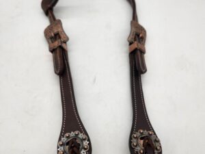 A leather headstall with intricate silver decorations and two buckles. The headstall features detailed stitching and metal accents. The background is plain white.