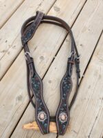 A detailed photo of a leather horse bridle with intricate turquoise and brown embroidery laid out on a wooden surface. The bridle features ornate designs and metal conchos, creating a visually striking piece of equestrian equipment.