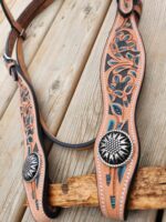 A detailed close-up of a Western-style leather belt adorned with intricate carvings and decorative metal conchos laid out on a wooden surface. The carvings feature floral and leaf patterns, with turquoise accents highlighting the design.