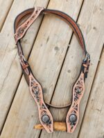 A leather headstall featuring intricate tooled designs and turquoise accents is laid out on a wooden surface. The design includes floral motifs and a central starburst pattern. The leather is natural colored with dark edges and metal buckles.