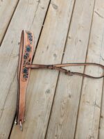 A leather dog leash with a matching collar featuring a floral pattern and turquoise accents is laid out on a wooden surface. The leash and collar are light brown, adorned with blue flowers and green leaves. The wood background has visible grain and knots.