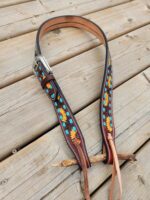 A handcrafted leather belt with a silver buckle lies on a wooden surface. The belt is decorated with painted sunflowers and turquoise accents, showcasing intricate and colorful detailing.