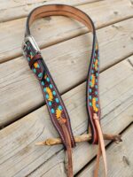 A handmade, dark brown leather belt adorned with colorful sunflower and turquoise bead designs is laid flat on a wooden surface. The belt features a silver buckle and leather lacing at the end.