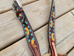 A handmade, dark brown leather belt adorned with colorful sunflower and turquoise bead designs is laid flat on a wooden surface. The belt features a silver buckle and leather lacing at the end.