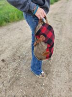 The Rocky Mountain Sling Bag- Explorer Series. The person is standing on a gravel path with green grass on the side. uNIQUE HIKING GEAR HIKING BAG OUTDOORSY