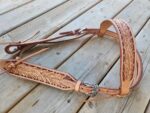 A detailed, ornate White Buckstitch Browband Headstall with intricate floral carvings and a silver buckle, displayed on a wooden surface. The belt style headstall features multiple leather straps and buckles. The craftsmanship highlights fine leatherwork with a rustic, Western aesthetic.