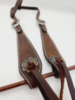 A pair of leather suspenders with silver buckles and decorative conchos on each strap. The suspenders are laid flat on a white surface, with leather detailing and white stitching visible along the edges.