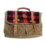 A rugged messenger bag with a brown waxed canvas body and a red and black plaid flap. The bag features leather straps and a handle, and has multiple pockets and compartments, creating a rustic and functional aesthetic.