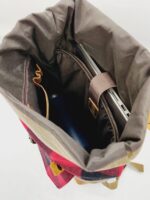 An open backpack shows a pocket holding a partial view of a laptop and a water bottle inside the main compartment. The interior is brown, and the exterior appears to have a red and beige plaid pattern.