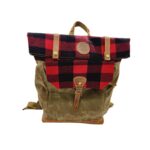 A stylish backpack featuring a red and black checkered top flap, secured with two brass buttons, and a buckle strap closure. The body of the backpack is made of olive green canvas with brown leather accents and adjustable straps.