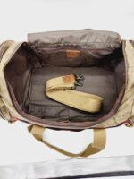 An open beige and brown travel bag is shown with its main compartment exposed. Inside, there is a detached beige shoulder strap with metal hooks. The bag has a zippered pocket on the inner side and two handles on either side at the top.