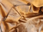 Close-up of a golden satin fabric with a soft, shiny surface. The fabric appears to be part of an interior lining, possibly of a piece of clothing or an accessory, with a visible pocket that is turned slightly outward. The material has a smooth and luxurious texture.