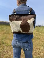 brown and white cowhide bag slung over their shoulder. cross body purse backpack hair on cowhide purse