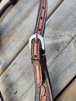 Close-up of a leather belt with decorative stitching, featuring a silver buckle. The belt is brown with a reddish-brown inner lining. The background consists of wooden planks with visible grain and texture.